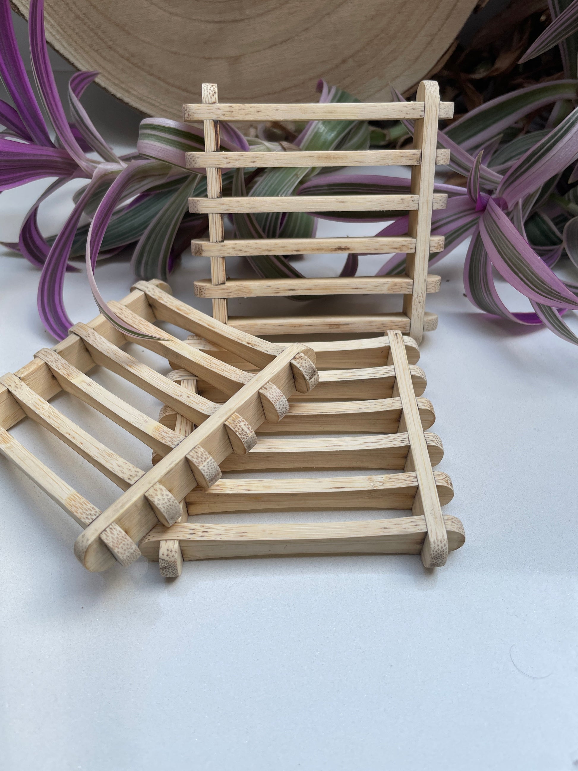 Three sustainable handmade bamboo soap dishes with foliage behind