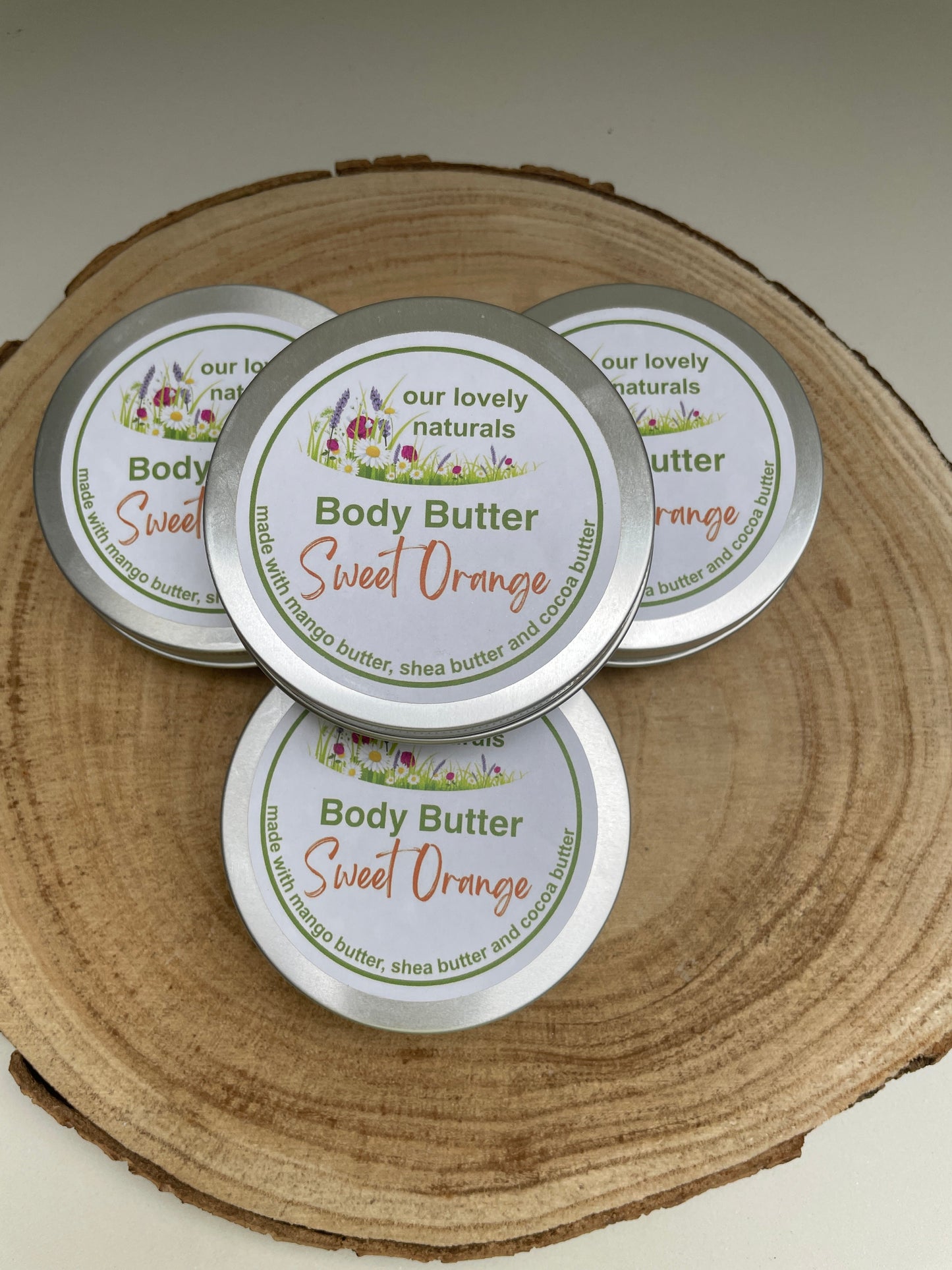 Four tins of completely natural, handmade, Sweet Orange body butter on a wooden board